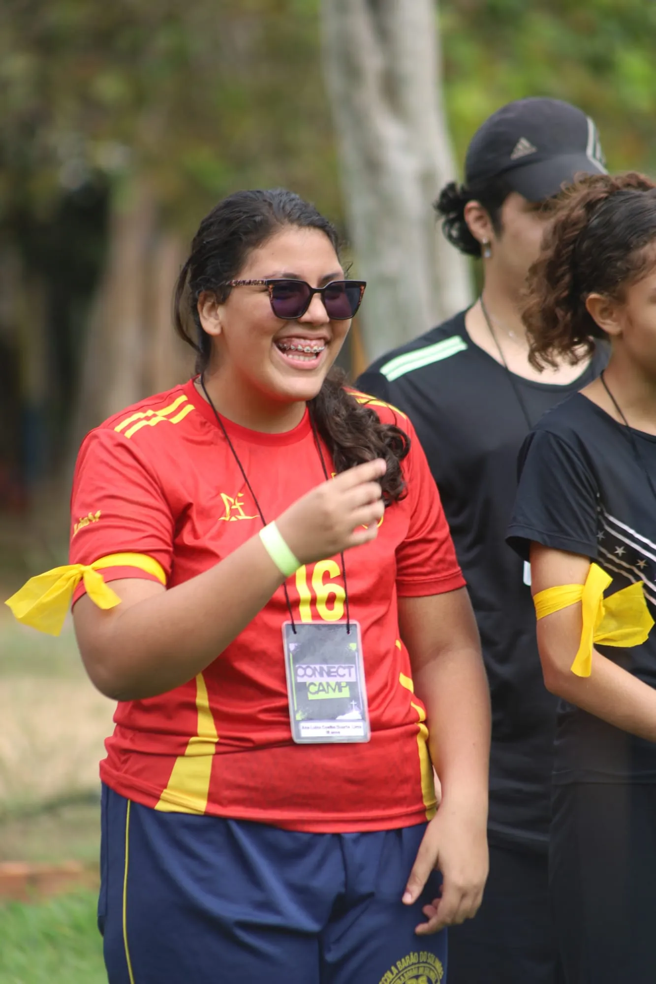 Jovem de óculos escuros e camiseta esportiva vermelha rindo durante as atividades ao ar livre