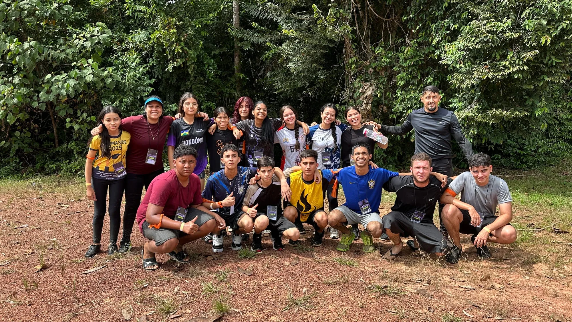 Grupo de jovens agachados posando juntos para foto em uma clareira na mata