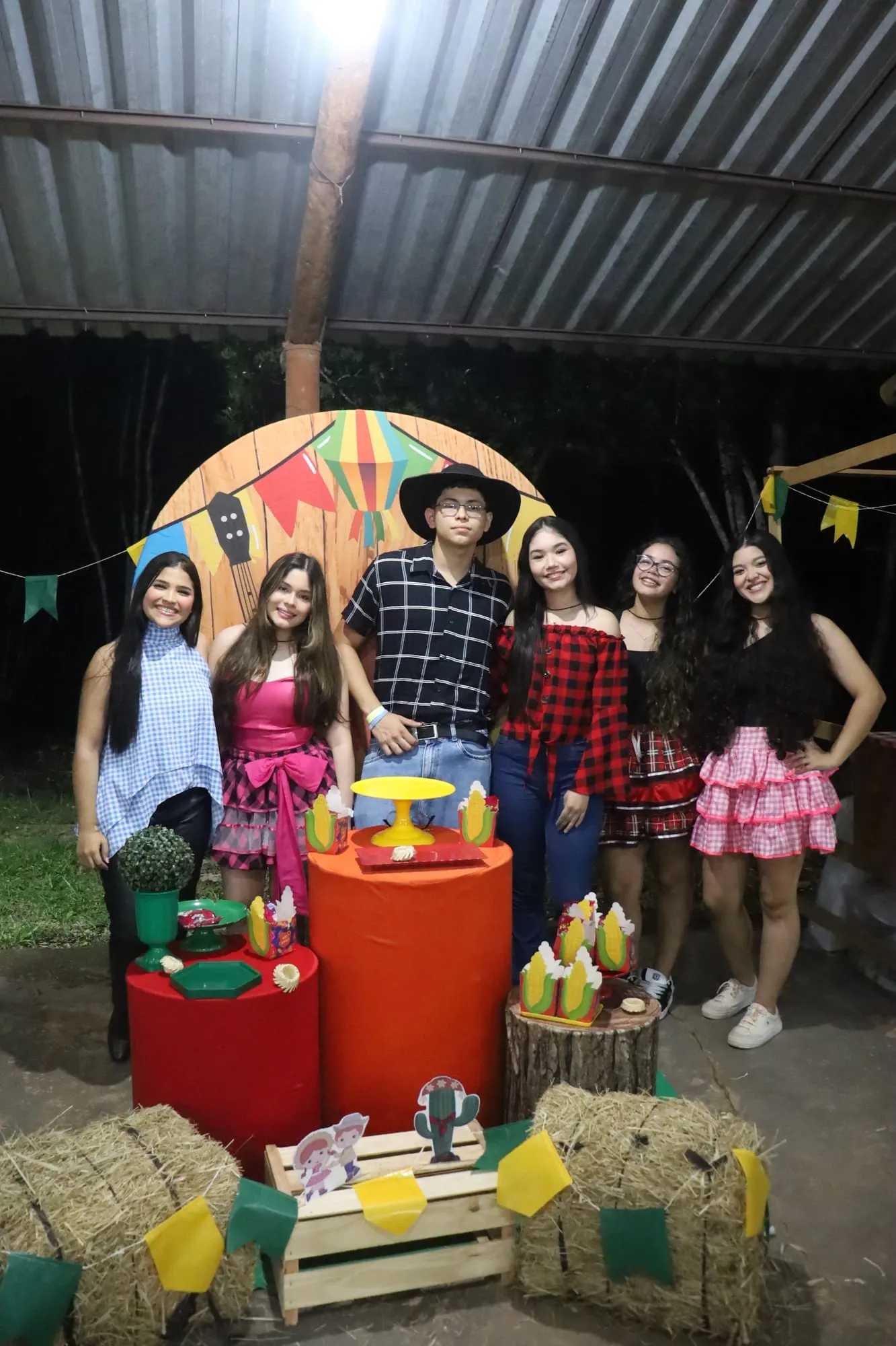 Grupo de jovens em trajes de festa junina posando diante da decoração colorida à noite