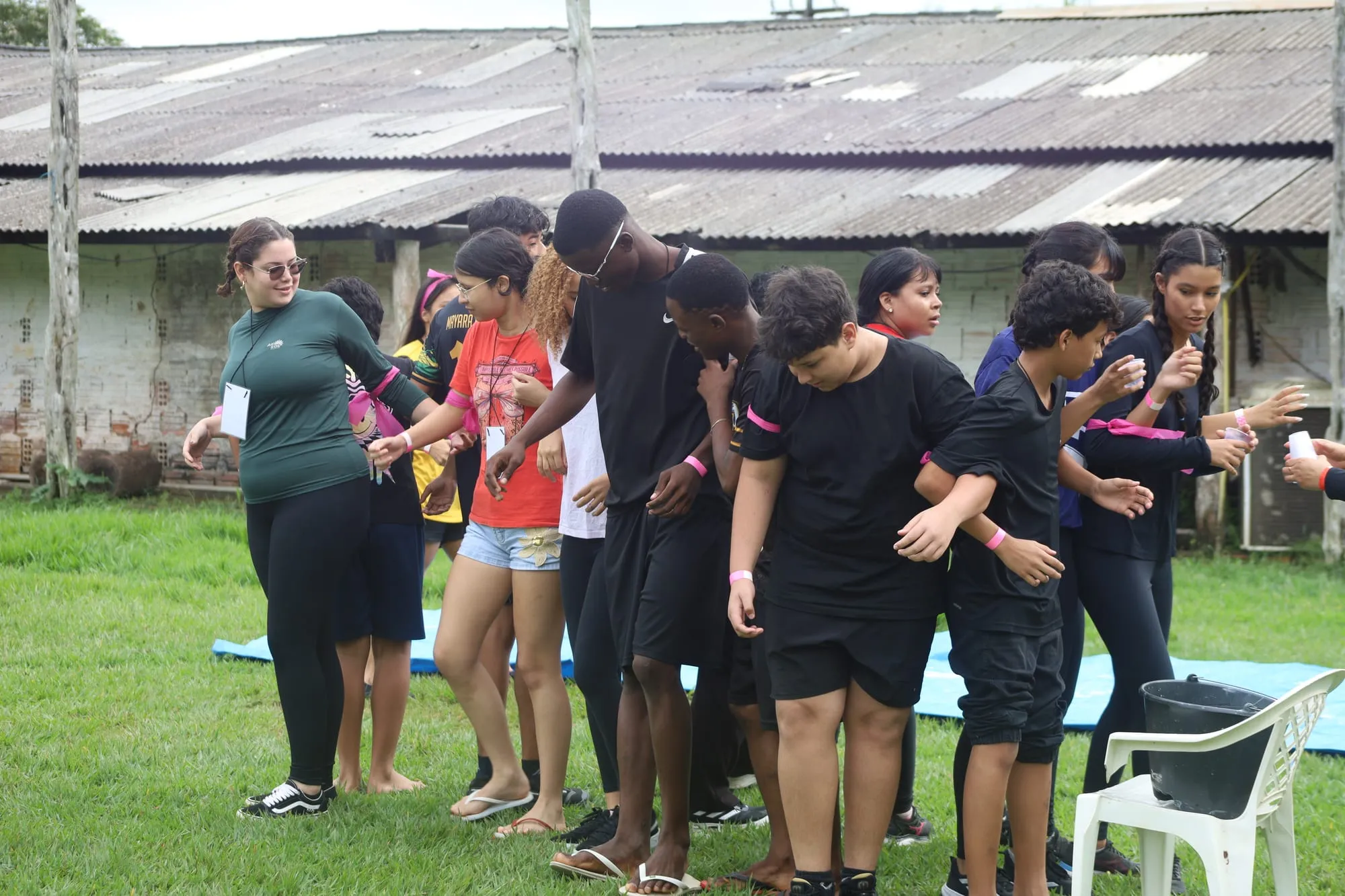 Jovens em fila numa brincadeira de equipe no gramado, apoiados uns nos ombros dos outros