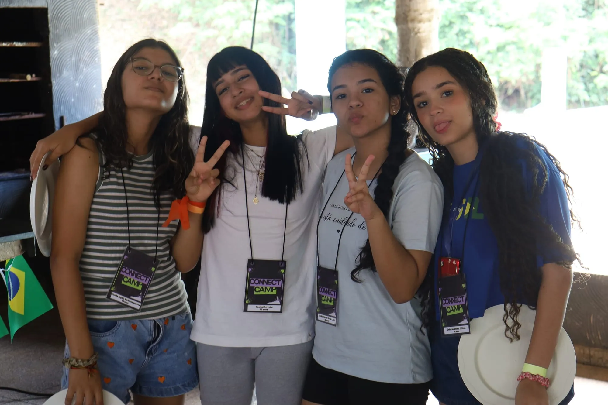 Quatro jovens sorrindo e fazendo sinal de paz com as mãos, usando os crachás do Connect Camp