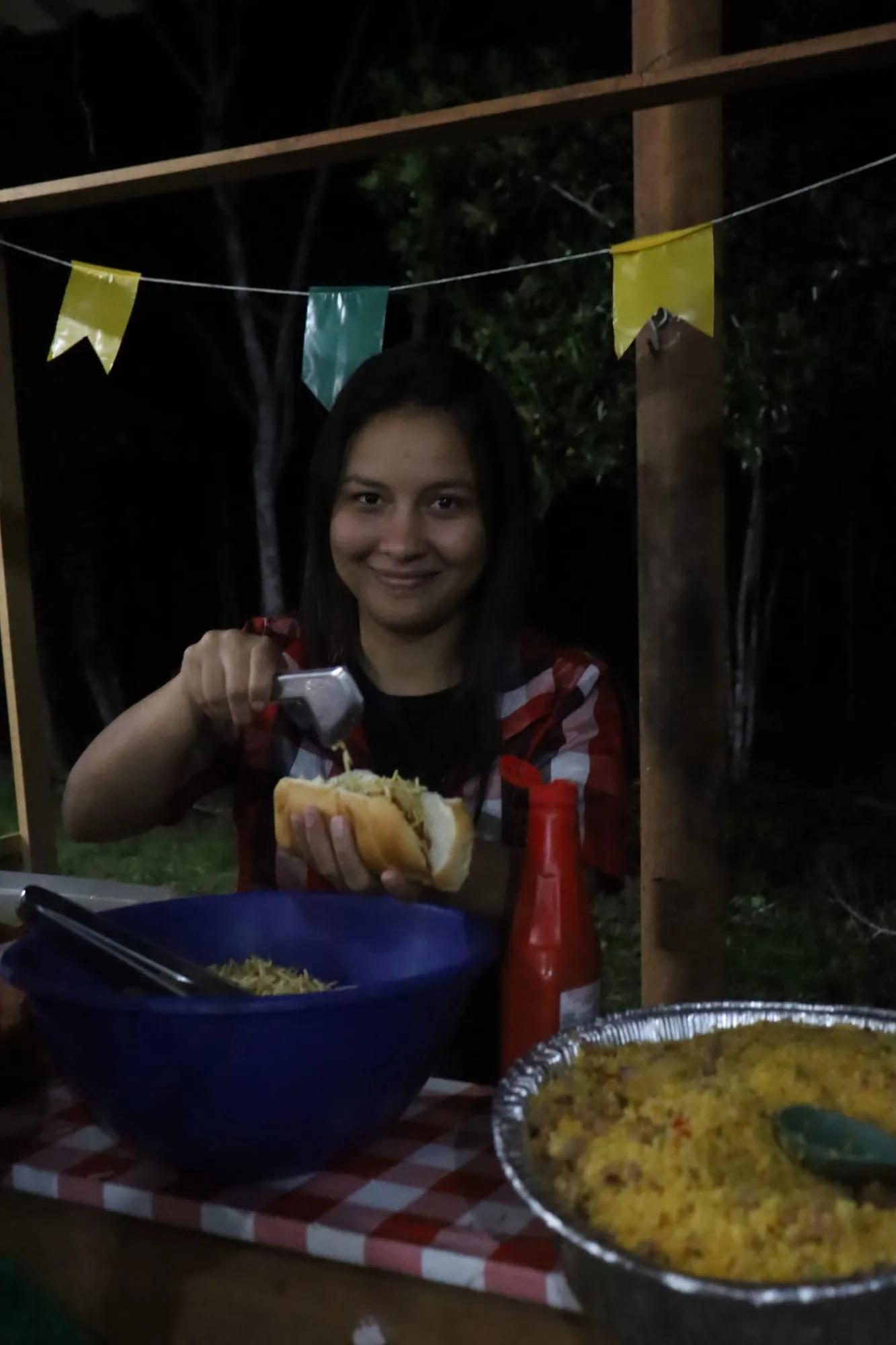 Jovem sorrindo enquanto monta um cachorro-quente na barraca de comida decorada à noite